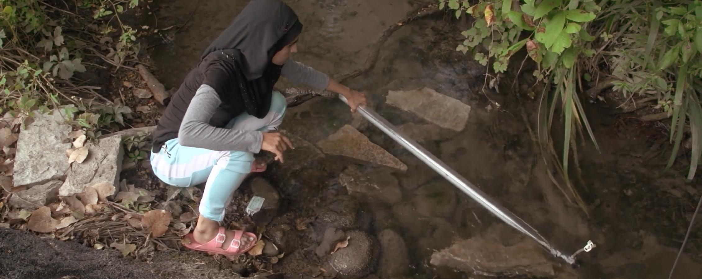 A student uses a tool to test water in a creek.