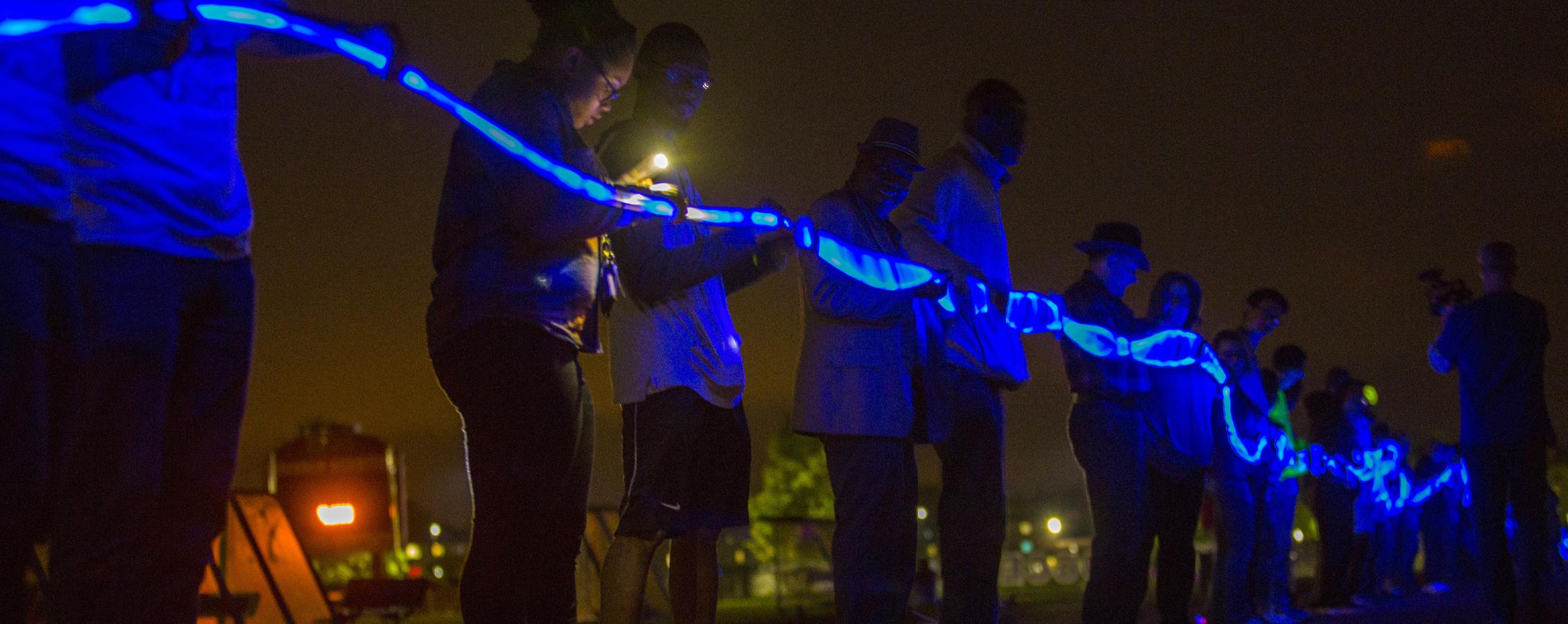 Students stand in a line outside holding a long blue glowstick.