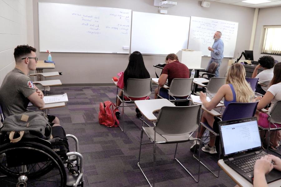 A lecturer stands in front of a white board.