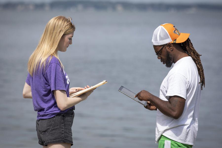 Two people talk while holding folders and a tablet.