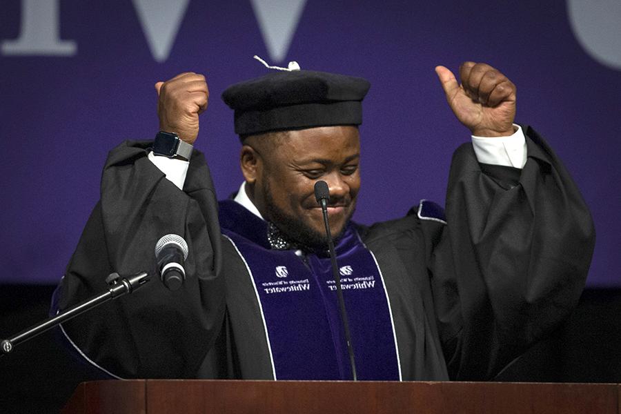 A person dressed in academic regalia smiles and throws their arms in the air at commencement.