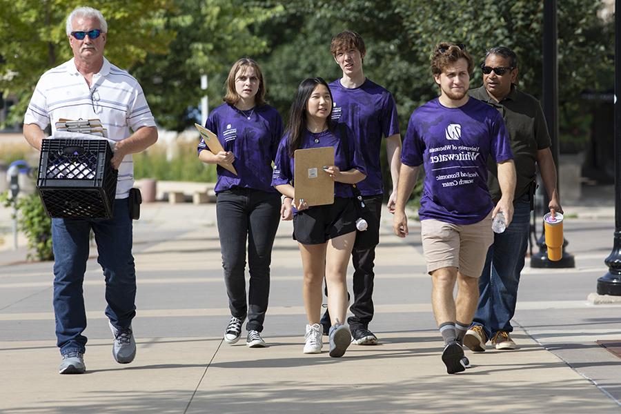 A group of students and a faculty member walk outdoors to collect information from people.