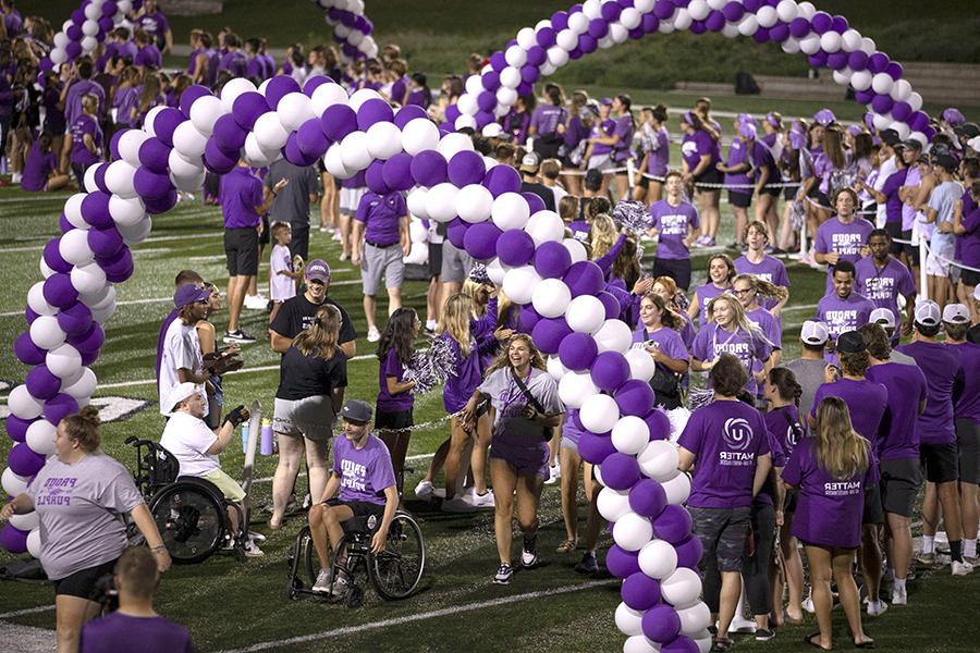 Two students walk past balloons on the football stadium.