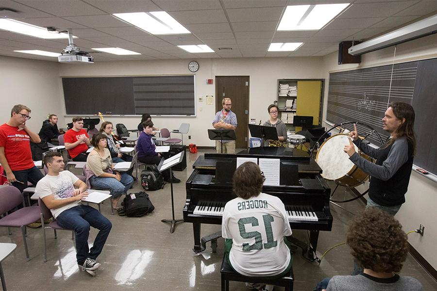 Jeff Herriott stands in front of his class of students with instruments in their hands.