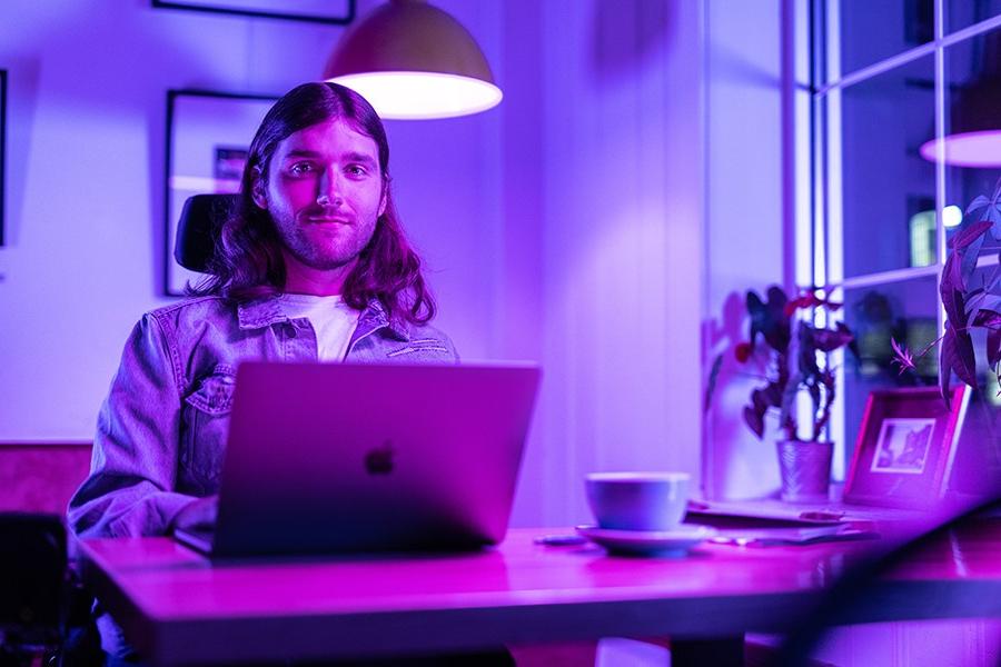 A person looks at the camera from behind a laptop.